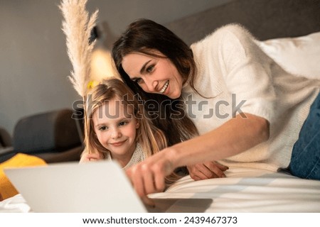 Mother and little girl using laptop watching funny cartoons together on bed