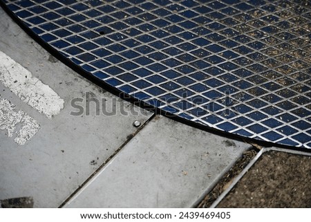 A close-up of a metallic grate against concrete, textures and patterns juxtaposed. Royalty-Free Stock Photo #2439469405
