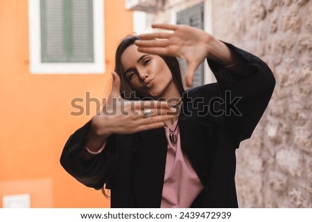Attractive woman with a lovely smile making a frame gesture with her fingers framing her face. Woman posing on selfie photo looking at camera walking outdoors in urban city, make blow kiss.