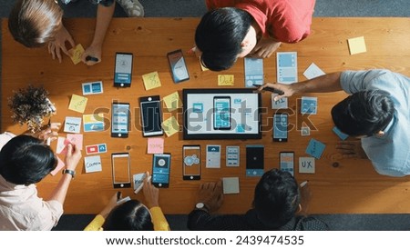 Top view of software developer team looking Ux Ui design for mobile phone interface from tablet while comparing and planning wireframe prototype designing together at creative workplace. Convocation.