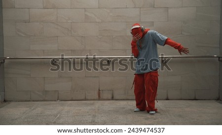 Handsome choreographer practice street dance in gray background. Young attractive b-boy dancer perform while wearing stylish cloth. Feeling of lively step. Copy space. Outdoor sport 2024. Sprightly.