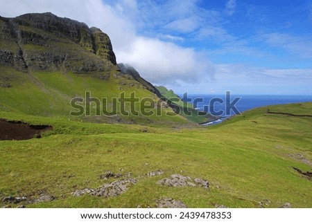 The deep blue of the North Atlantic Ocean frames the rugged, raw beauty of the mountainous, uninhabited north coast of Vagar, Faroe Islands