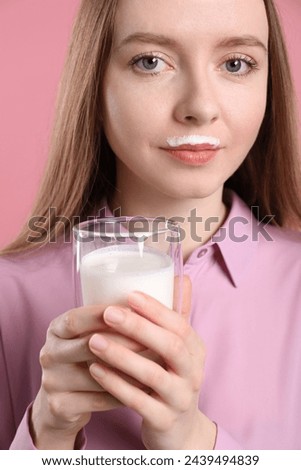 Cute woman with milk mustache holding glass of tasty dairy drink on pink background