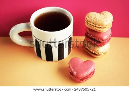 Heart-shaped macarons next to a cup of tea on a pink and yellow background