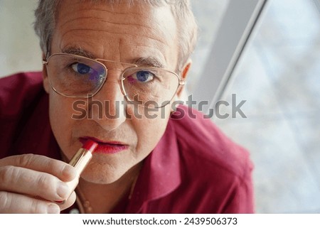 A gay man putting on makeup with glasses and a serious expression. new masculinity Royalty-Free Stock Photo #2439506373