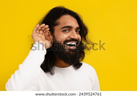 Curious interested millennial indian man holding hand near ear and trying to hear information, yellow studio background, copy space. Excited eastern guy in casual clothing eavesdropping Royalty-Free Stock Photo #2439524761