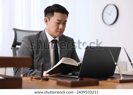 Notary working with laptop and book at wooden table in office