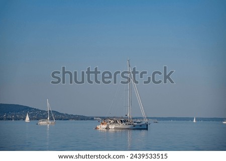 Sailboats anchored next to each other on the waters of Lake Balaton along the shore with the hills of the Bakony in the background