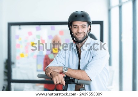 Portrait of smiling businessman riding electric scooter in office with colleague in background