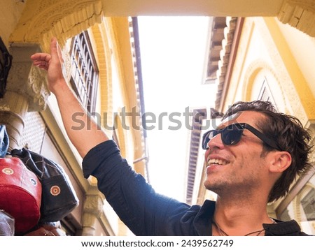 Smiling handsome man with sunglasses and black shirt at handicraft market in Granada Spain pointing up left Royalty-Free Stock Photo #2439562749
