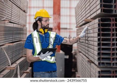 Caucasian engineer with yellow hardhat inspect steel bars with tablet in a factory
