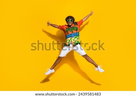 Full length photo of eccentric guy wear hawaii shirt sneakers in glasses raising arms up jumping isolated on yellow color background
