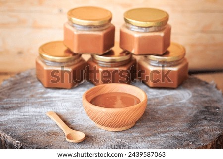 Boiled, condensed milk in a wooden plate, close-up against the background of glass jars filled with condensed milk, food photography, wooden background, milk products.