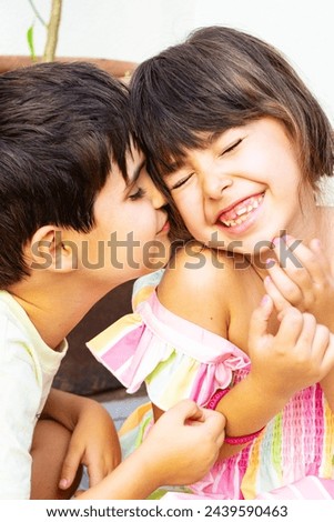 Love between siblings. Portrait of a 7 years child boy giving a kiss to his smiling sister, a 6 years old girl, Caucasian. Vertical.