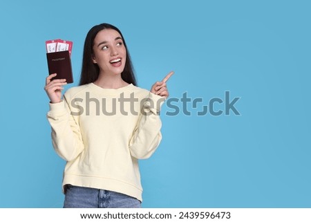 Happy woman with passport and tickets pointing at something on light blue background. Space for text