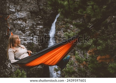 Summer vacations - woman chilling in hammock in forest travel outdoor tourist girl enjoying waterfall view in Norway adventure trip healthy lifestyle with camping gear weekend bivouac in wilderness 