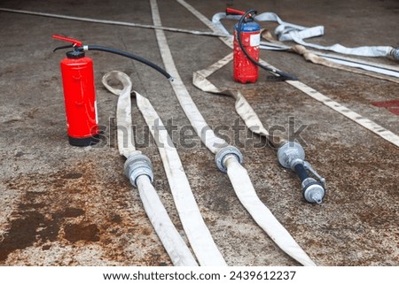 Red fire extinguisher cylinder with unwound fire hoses. Royalty-Free Stock Photo #2439612237