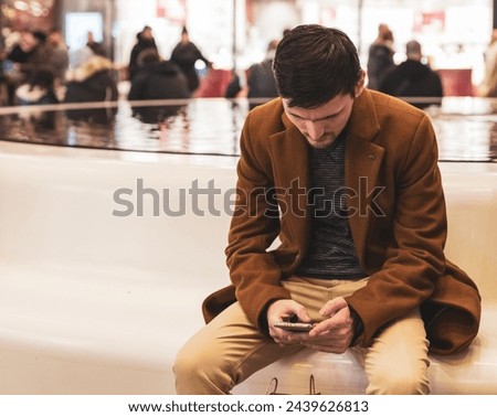 A young man with a phone in his hands is sitting on a bench in a store.
