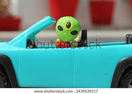 Plastic alien toy driving a plastic car toy at sunny day. 