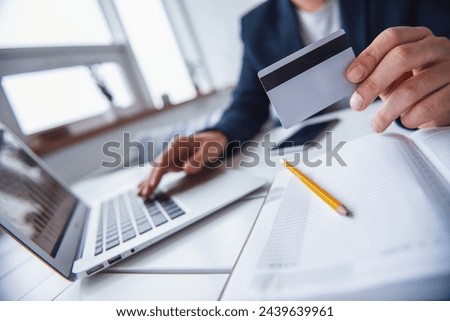 Cropped image of young businessman with long dark hair holding a credit card while working with a laptop in a cafe