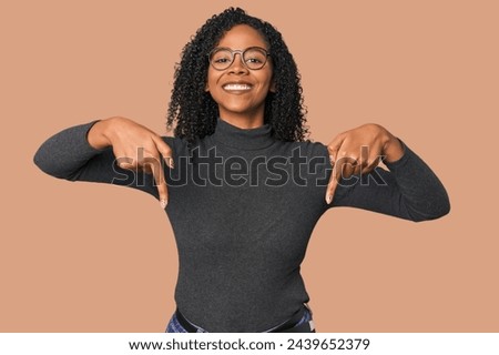 African American woman in studio setting points down with fingers, positive feeling.