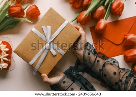 Gift box with a bow and tulips in the hands of a girl, festive background.