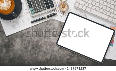 An organized desk featuring a blank tablet screen, financial documents, a cup of cappuccino, and office supplies.
