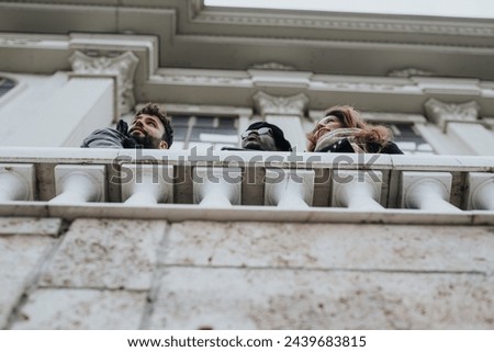 Three friends looking upwards from balcony of historic building, candid moment. Royalty-Free Stock Photo #2439683815