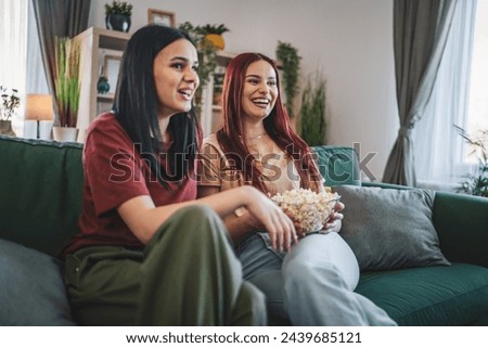 two women caucasian teenage friends or sisters watch movie tv series at home sit on sofa bed with popcorn