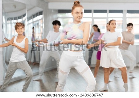 Teenagers in classroom dance and learn modern dances, participants of lesson move in staggered manner to beat of energetic music. Female teacher in background dances with students