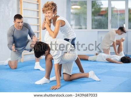 Concentrated teen boys practicing armlock, painful control move to hold and immobilize opponent, in training bout during self defence course with male trainer in gym .. Royalty-Free Stock Photo #2439687033
