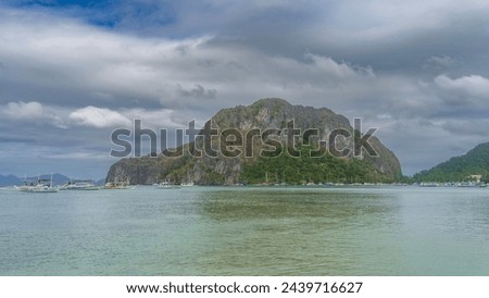 Many yachts, sailboats, and traditional Filipino double-outrigger dugout bangka boats are moored and anchored in the calm bay. A picturesque mountain with green vegetation on steep rocky slopes  Royalty-Free Stock Photo #2439716627