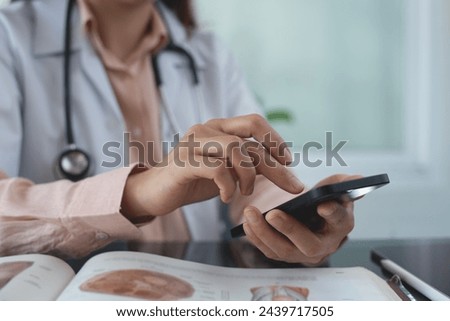 Asian doctor using smartphone for wellness research, medical app and online consulting, Medical student using mobile phone with anatomy book on table at medical school