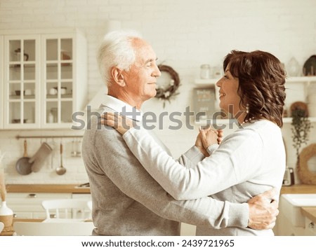 A beautiful elderly married couple is dancing in the room. Pensioners are happy together.