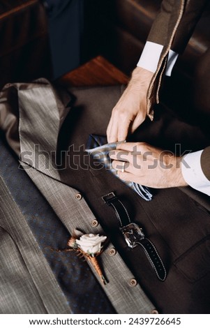 Groomsman folds a handkerchief on groom suit next to the boutonniere Royalty-Free Stock Photo #2439726645