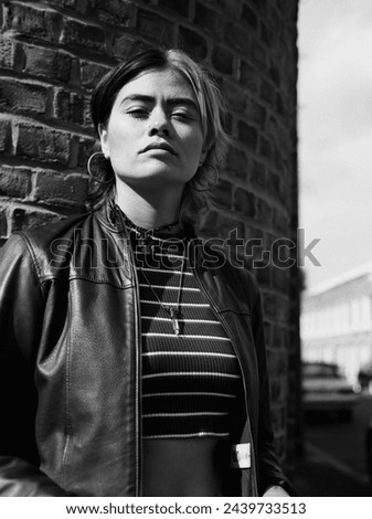 Arrogant mixed race woman posing in the street in a black and white portrait. Image taken with a medium format analog film camera. She is leaning against a brick wall in a sunny day.