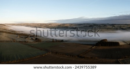 Aerial view of low lying mist or cloud inversion along the River Tyne valley at Haydon Bridge near Hexham on a cold Winter morning Royalty-Free Stock Photo #2439755389