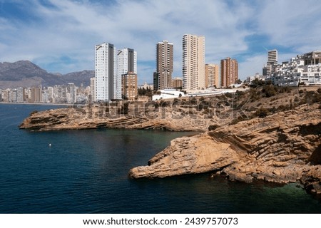 Aerial drone photo of the north part of Benidorm in Spain showing the rocky paths by the ocean and the high rise apartments on a sunny day in the summer time.