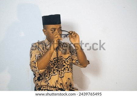 Asian man wearing a batik sarong and cap poses confidently in an isolated photo. Comercial photo for ramadhan or ied mubarak theme.