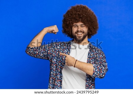 I am strong and independent. Man with Afro hairstyle wig showing biceps and looking confident, feeling power strength to fight for rights, energy to gain success win. Guy isolated on blue background Royalty-Free Stock Photo #2439795249