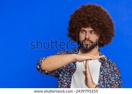 Tired serious upset man with Afro hairstyle wig showing time out gesture, limit or stop sign, no pressure, I need more time, take a break, relax rest, help. Guy isolated on blue background. Copy-space Royalty-Free Stock Photo #2439795255