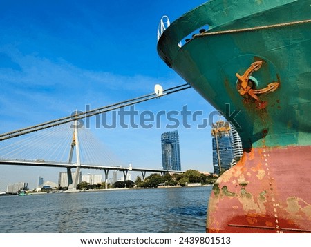 Anchor on large cargo ship's anchor being pulled. Green and red ship, While docked at the pier by large ropes on the river, in the background is a view of the bridge buildings and transport concept