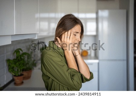 Tired woman feeling headache rubbing temples standing on kitchen with closed eyes at home. Blonde female suffering from migraine head pain. Having headache cephalalgia premenstrual syndrome feel bad.  Royalty-Free Stock Photo #2439814911