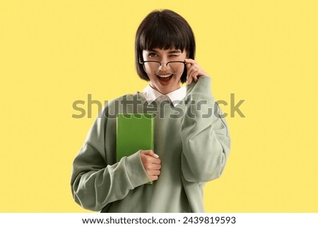 Happy young woman in eyeglasses with book on yellow background