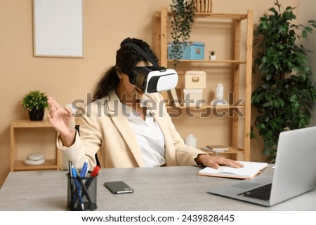 Young African-American businesswoman in VR glasses working at table in office