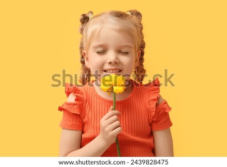 Cute little girl with beautiful yellow ranunculus flower on color background