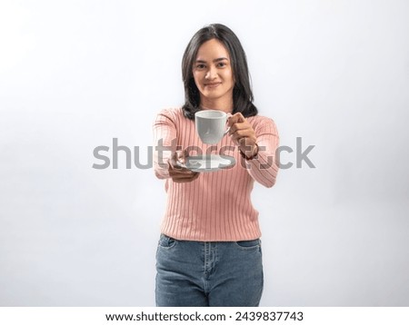 Portrait of an Indonesian Asian woman, wearing a pink sweater, enjoying a drink with a cup, isolated against a white background.