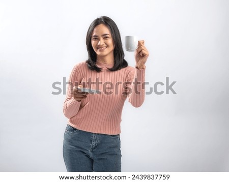 Portrait of an Indonesian Asian woman, wearing a pink sweater, enjoying a drink with a cup, isolated against a white background. Royalty-Free Stock Photo #2439837759