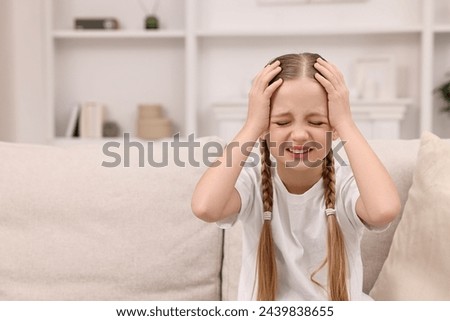 Little girl suffering from headache at home. Space for text