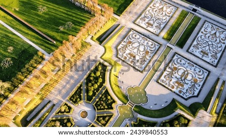 Aerial view of the ornate and symmetrically designed gardens of Hillerød Castle in Denmark, captured in the warm light of the sun, highlighting the intricate patterns and landscaping artistry